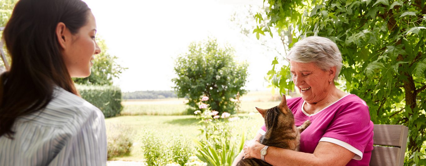Ältere Dame mit Katze im Garten.
