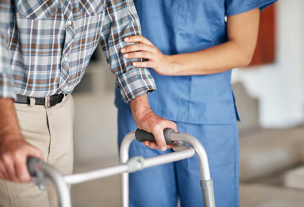 Eine Pflegekraft untersützt einen älteren Mann beim Laufen.