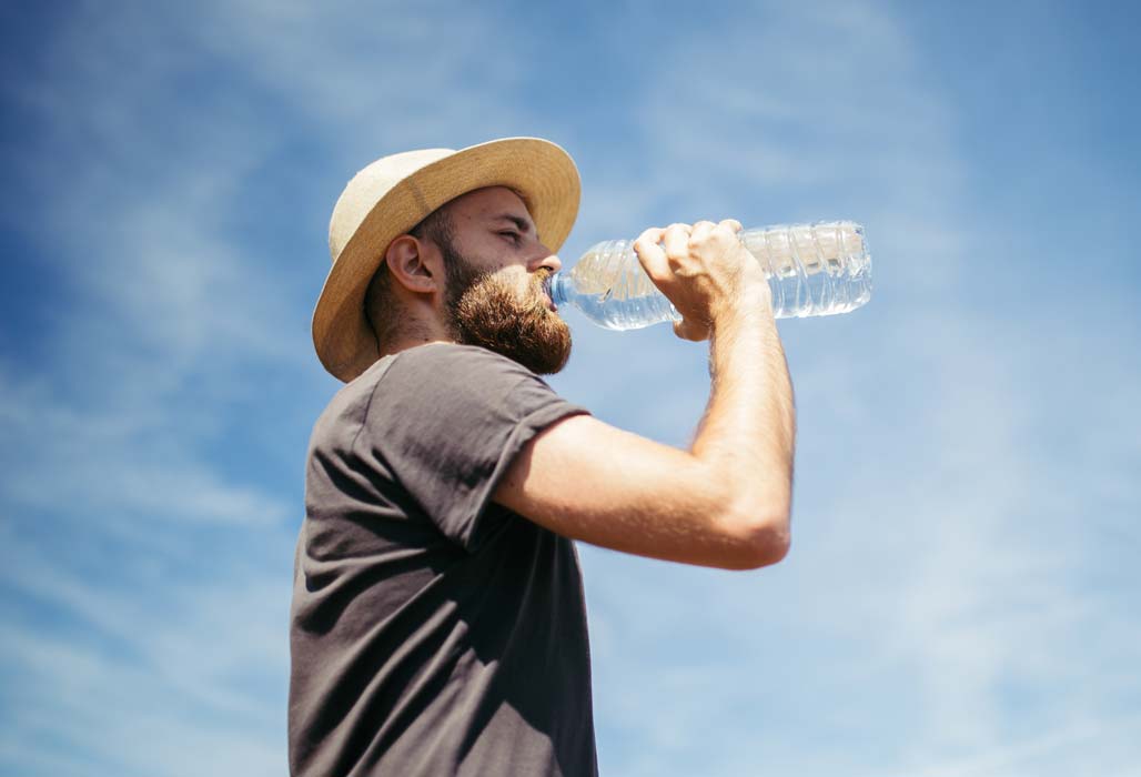 Hitze - Mann mit Hut trinkt aus einer Wasserflasche
