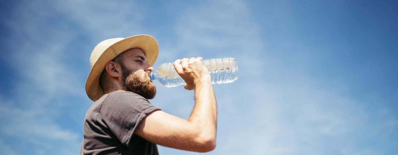 Mann mit Hut trinkt aus einer Wasserflasche