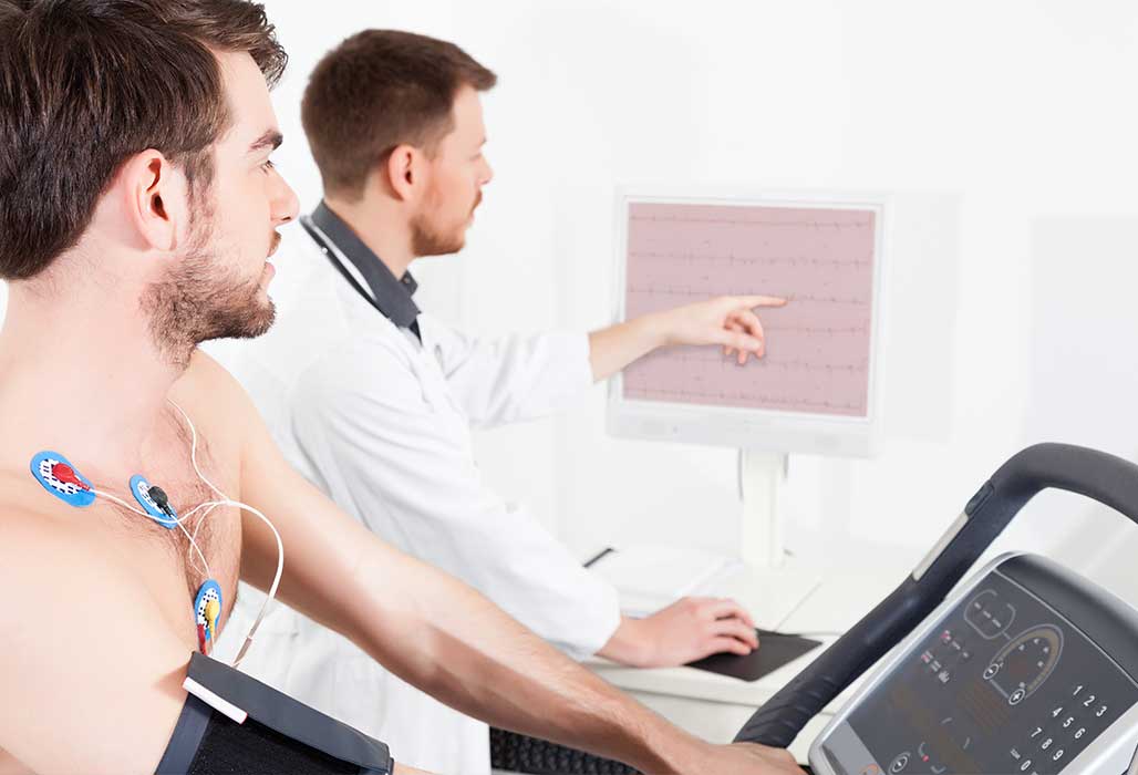Arzt deutet auf einen Monitor mit Werten, während ein junger Mann ein Belastungs-EKG durchführt